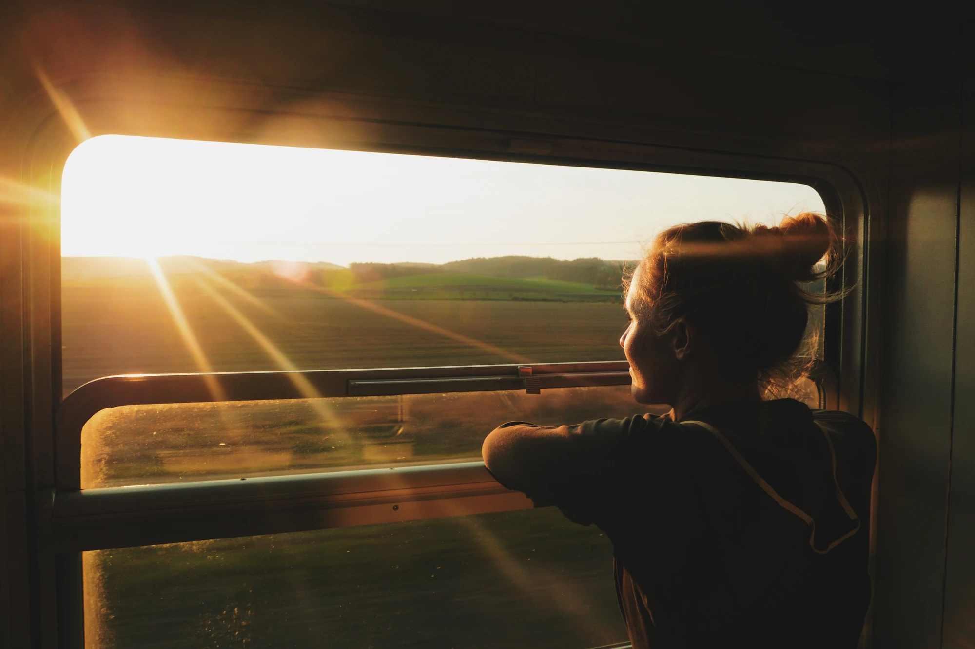 Frau beobachtet die Landschaft bei Sonnenuntergang aus dem Zugfenster