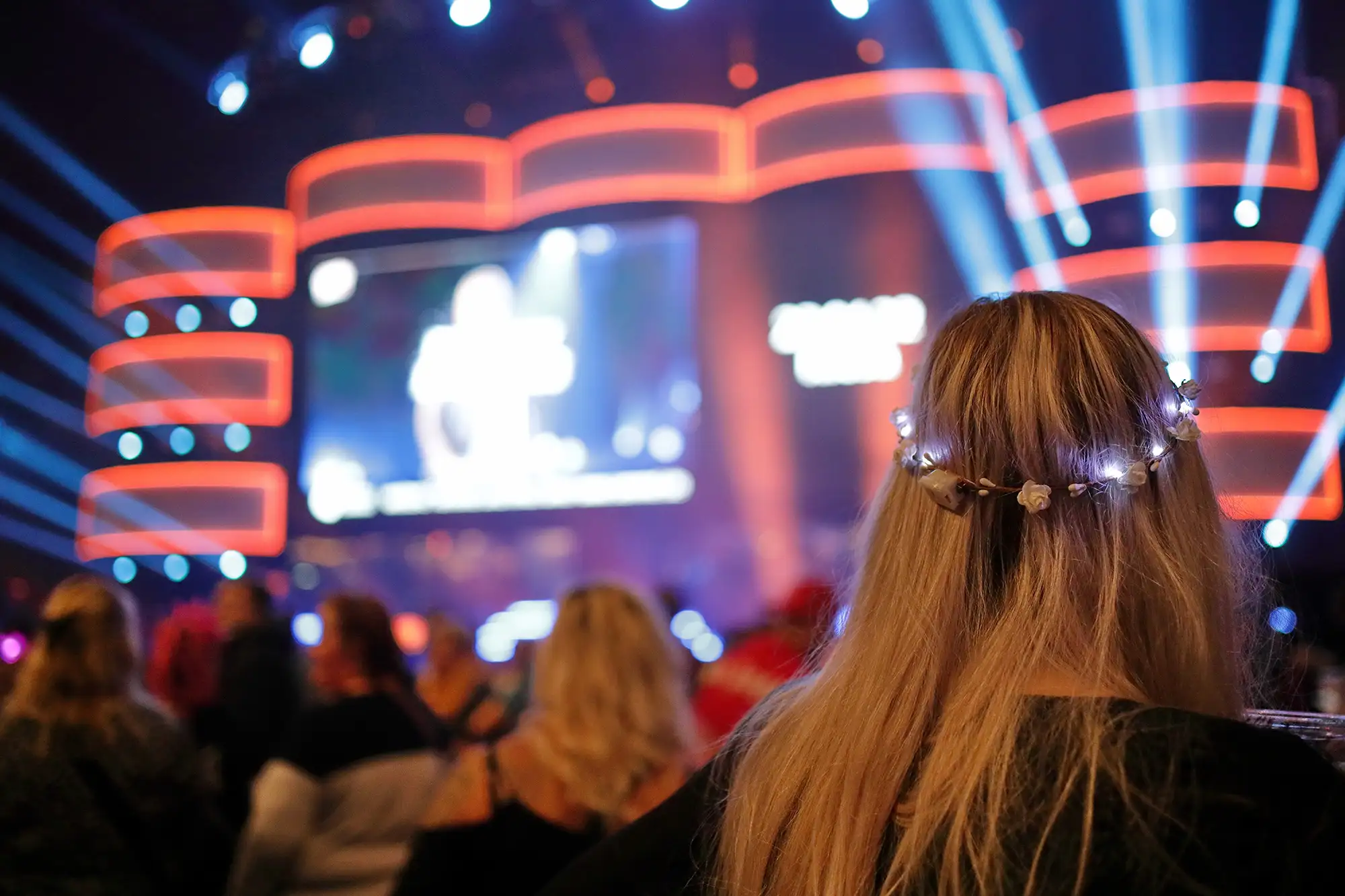 Eine Frau mit einem Haarband im Publikum vor einer bunt beleuchteten Bühne