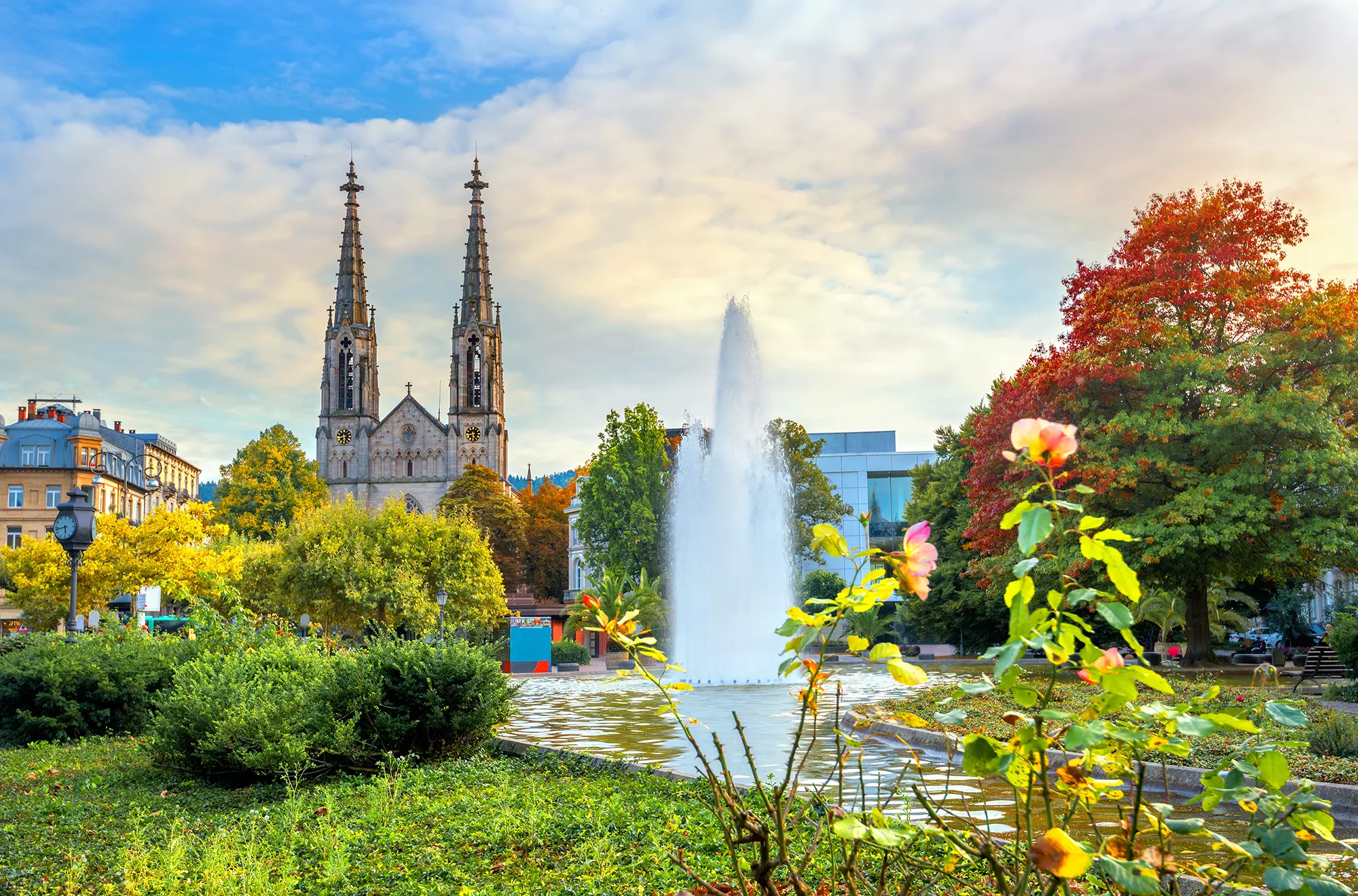 Evangelische Kirche in Baden-Baden hinter einem Springbrunnen mit Fontäne und herbstlichem Baum mit bunten Blättern