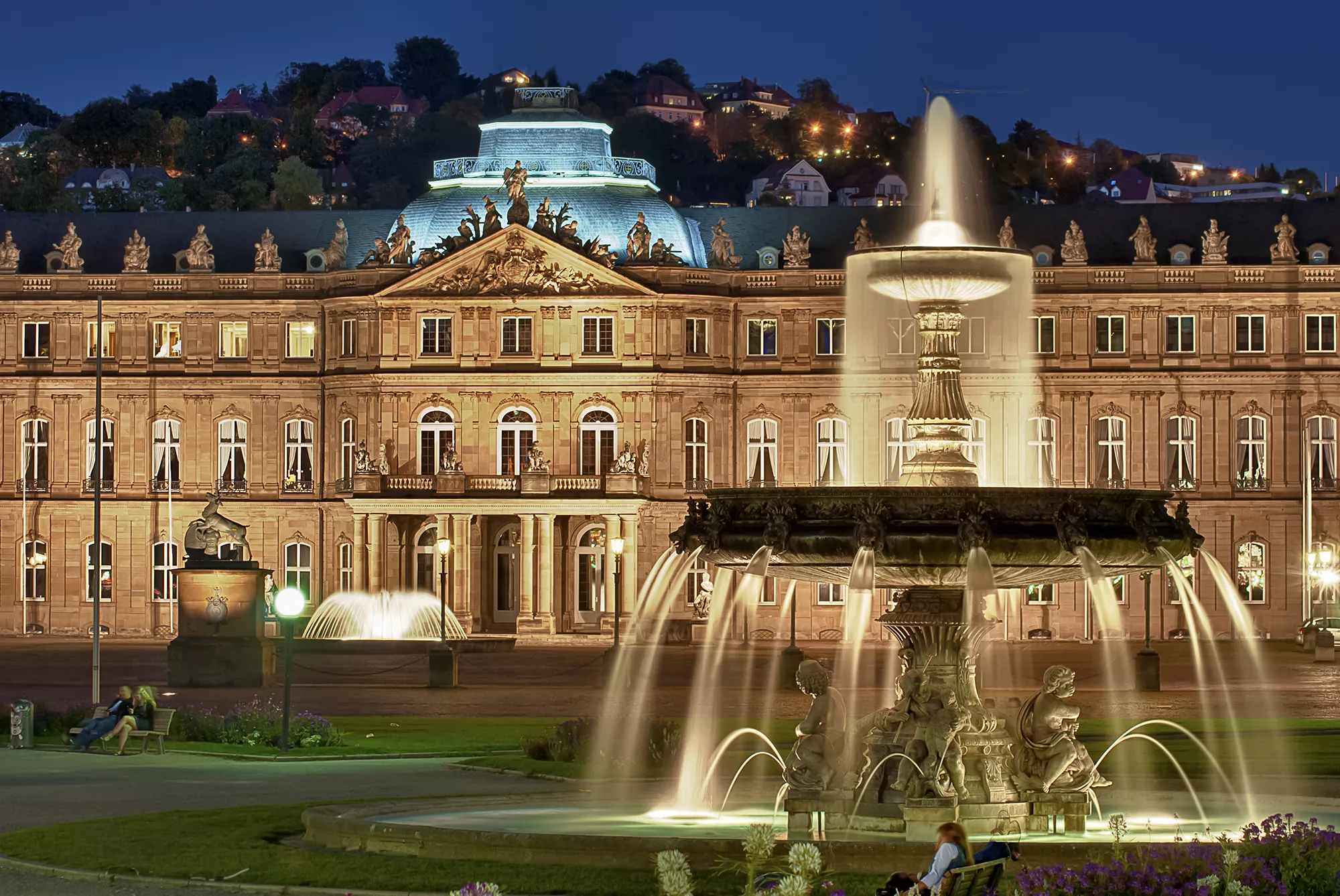 Blick auf das illuminierte Neue Schloss mit Brunnen in der Abenddämmerung bei einer Städtereise Stuttgart