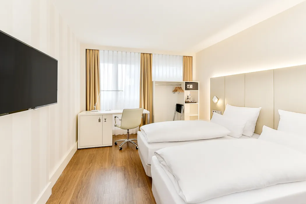 NH Hotel Erlangen - geräumiges weißes Zimmer mit getrennten Betten, Tisch, Stuhl, Garderobe, TV
