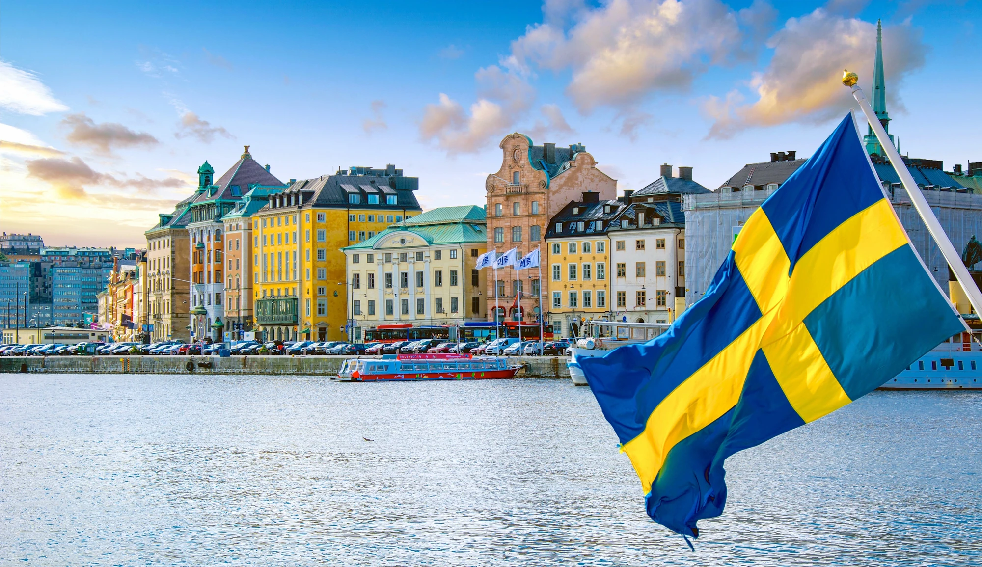 Blick vom Boot auf schwedische Flagge mit Altstadt im Hintergrund bei Städtereise Stockholm Urlaub